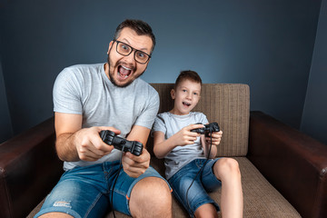 A cheerful family, dad mom and son play on the console, video games, emotionally react sitting on the couch. Day off, entertainment, leisure, spend time together.