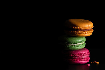 Colorful macaroons on dark black background. Variety of french almond macaron cookies in pile. Dessert, sugar, bakery creative concept. Macro shot, side view, close up, copy space. Low key