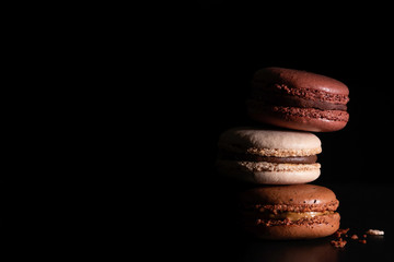 Fototapeta na wymiar Colorful chocolate macaroons on dark black background. Variety of french almond macaron cookies in pile. Dessert, sugar, bakery creative concept. Macro shot, side view, close up, copy space. Low key