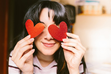 Happy brunette woman with red glitter heart shaped cardboard in her eyes smiling on valentines day. Valentine's day and fall in love concept.
