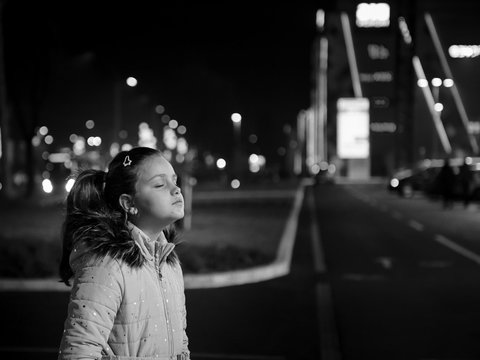 Little girl with closed eyes staying in dark in front of shopping mall lights