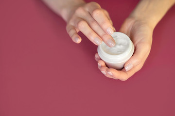 Woman holds hand cream, girl holds a jar of cream on a pink background