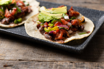 Mexican pork chorizo tacos with avocado and beans on wooden background