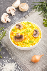 Yellow fried rice with champignons mushrooms, turmeric and oregano in white ceramic bowl on a black concrete background. side view.