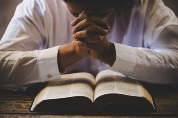 Hands folded in prayer on a Holy Bible in church concept for faith