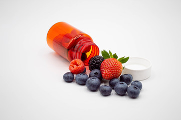 Strawberries, raspberries, blackberries, and blueberries pouring from medicine bottle with cap