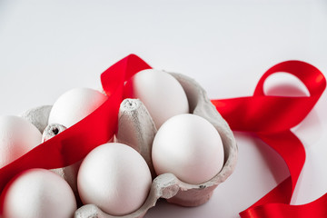 Easter eggs in a cardboard box with a red festive ribbon on a white background.