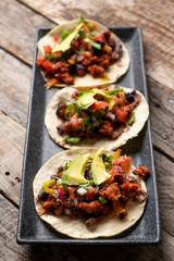 Mexican pork chorizo tacos with avocado and beans on wooden background