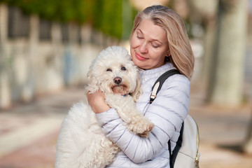 middle-aged woman walking with fluffy white dog in summer city