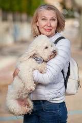 middle-aged woman walking with fluffy white dog in summer city