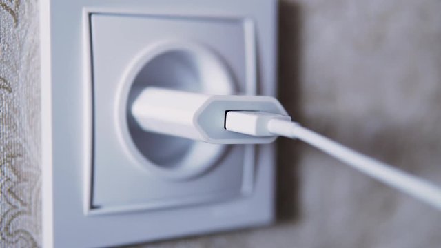 Man hand plug in charger adapter into wall socket close up