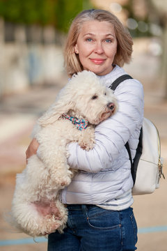 Middle-aged Woman Walking With Fluffy White Dog In Summer City