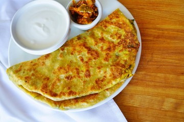 A plate with aloo paratha bread stuffed with potatoes and a dish of yogurt at an Indian restaurant