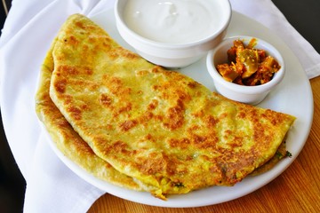 A plate with aloo paratha bread stuffed with potatoes and a dish of yogurt at an Indian restaurant