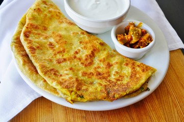 A plate with aloo paratha bread stuffed with potatoes and a dish of yogurt at an Indian restaurant