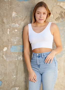 Beautiful young Latina woman posing in desert wearing white tank top and jeans - agains weathered concrete wall