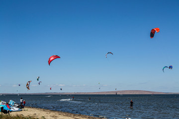 Colorful kiteboard parachutes in the sky. Kitesurfing, Kiteboarding, Kiteboarders competitions concept. Kitesurfers surfing the wind on waves on bright sunny summer day. Many of kites in the blue sky