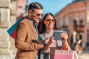 Couple with shopping bags watching something on tablet