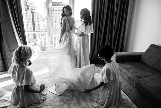 Bride's preparation. Bridesmaids are straighten brides dress. Black and white photo