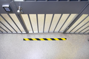 Metal bar security door in the bank with an electronic lock with keypad and steel bobble handle. Do not cross yellow sign on the floor. 