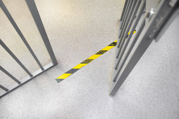 Opened metal grey bar in prison. Yellow do not cross tape on the floor.