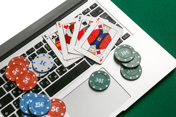 Chips and playing cards for gambling games with laptop on table, closeup