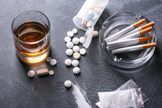 Glass of whiskey with cigarettes and drugs on dark background