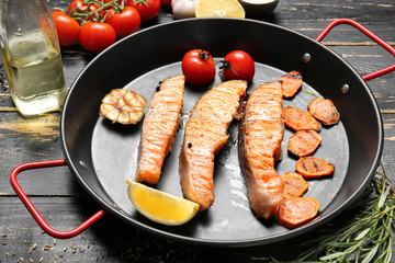 Frying pan with tasty cooked salmon and vegetables on table