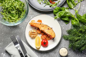 Plate with tasty cooked salmon and vegetables on grey background