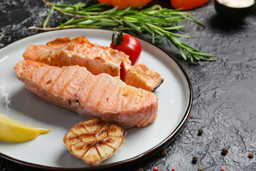 Plate with tasty cooked salmon and vegetables on dark background