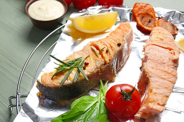 Cooling rack with tasty cooked salmon and vegetables on table, closeup