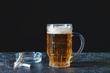Mug of beer with cigarettes on table. Concept of alcoholism
