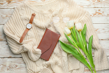 Wallet with sweater, clock and flowers on white wooden background