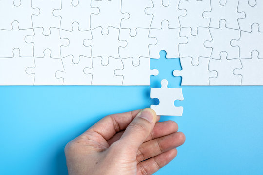 Hand Putting The Last Piece Of White Jigsaw Puzzle On Blue Background And Place For Your Content