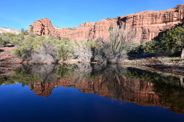 Fototapeta na wymiar Red rock formations reflected in tranquil pond in Sedona, Arizona backcountry on clear cloudless winter afternoon.