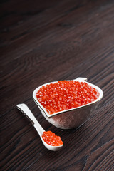 Red caviar in a white ceramic bowl with spoon on a brown rustic wooden background
