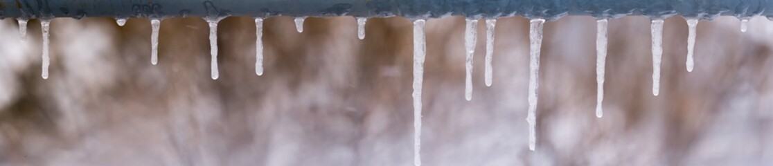 panoramic view of icicles on snow bokeh background. icicles on a metal crossbar