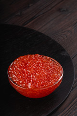 Red caviar in a glass bowl on a dark wooden table