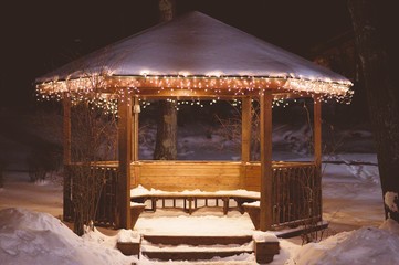 Wooden gazebo covered with snow and decorated with lights at night - Powered by Adobe