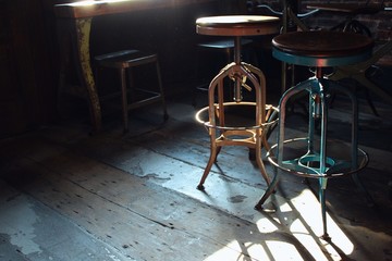 Fototapeta na wymiar Interior of a typical vintage style cafe with shabby wooden floors and furniture, industrial style metal bar chairs in bright sunlight that contrasts with sharp shadows in the corners.