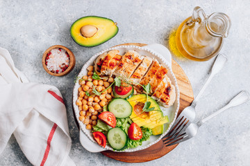Healthy vegetable buddha bowl lunch with grilled chicken and chickpeas, cucumber, tomato and avocado on light gray background. Top view. Zero waste concept