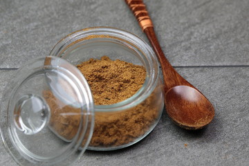 An Indian spice powder which is made of Roasted Cumin seeds in a jar on grey background.