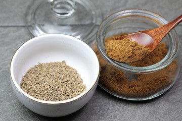 An Indian spice powder which is made of Roasted Cumin seeds in a jar on grey background.