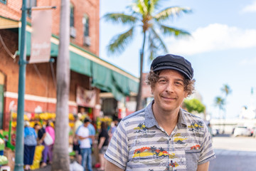 A man wearing a Hawaiian shirt and sailor hat enjoys the day exploring a farmers market in Hawaii.