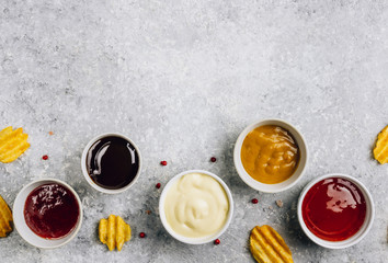 Obraz na płótnie Canvas White bowls of various dip sauces on gray background. Mustard, ketchup, cheese, teriyaki and cranberries sauces. Top view with copy space. Flat lay