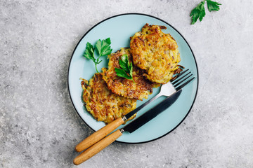Homemade potato pancakes or hash brown on blue plate with sauce on gray table. Traditional dish in European and American cuisine. Top view.