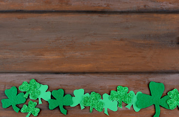 Saint Patrick's Day image of glittered nad felt green sharmocks forming a border  on a rustic wooden background.