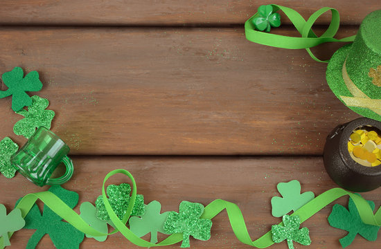 Saint Patrick's Day image of glittered green and felt sharmocks woth ribbon form a border on a rustic wooden background. Leprechaun hat and pot of gold included.