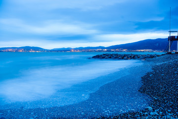 Gelendzhik beach in the evening in a storm. The waves at high speed turn into a blue fog. Blue tones, winter. Pebble beach, breakwater. In the background, the Caucasus mountains. 