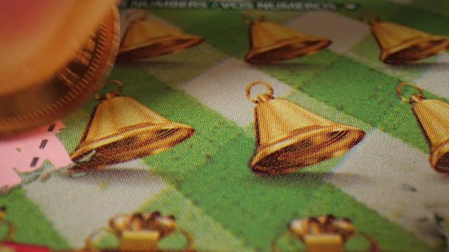 Close-up of using a lucky penny to scratch off an instant lottery ticket with bell symbols.